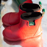 Pair of Kids Little Green Radicals Ankle Wellies in Red - made from Fair Trade Rubber - flexible with gripped soles - sat in a puddle.