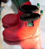 Pair of Kids Little Green Radicals Ankle Wellies in Red - made from Fair Trade Rubber - flexible with gripped soles - sat in a puddle.