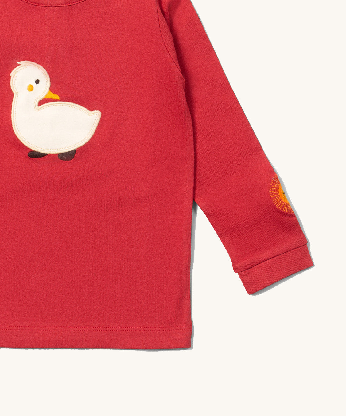 A close up of the Little Green Radicals duckling applique long sleeve top available at Babipur showing the sun embroidery and white duckling applique detail on  red organic cotton fabric.
