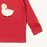 A close up of the Little Green Radicals duckling applique long sleeve top available at Babipur showing the sun embroidery and white duckling applique detail on  red organic cotton fabric.