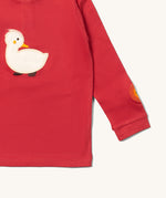 A close up of the Little Green Radicals duckling applique long sleeve top available at Babipur showing the sun embroidery and white duckling applique detail on  red organic cotton fabric.