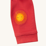 A close up of the Little Green Radicals duckling applique long sleeve top available at Babipur showing the sun embroidery detail on red organic cotton fabric.