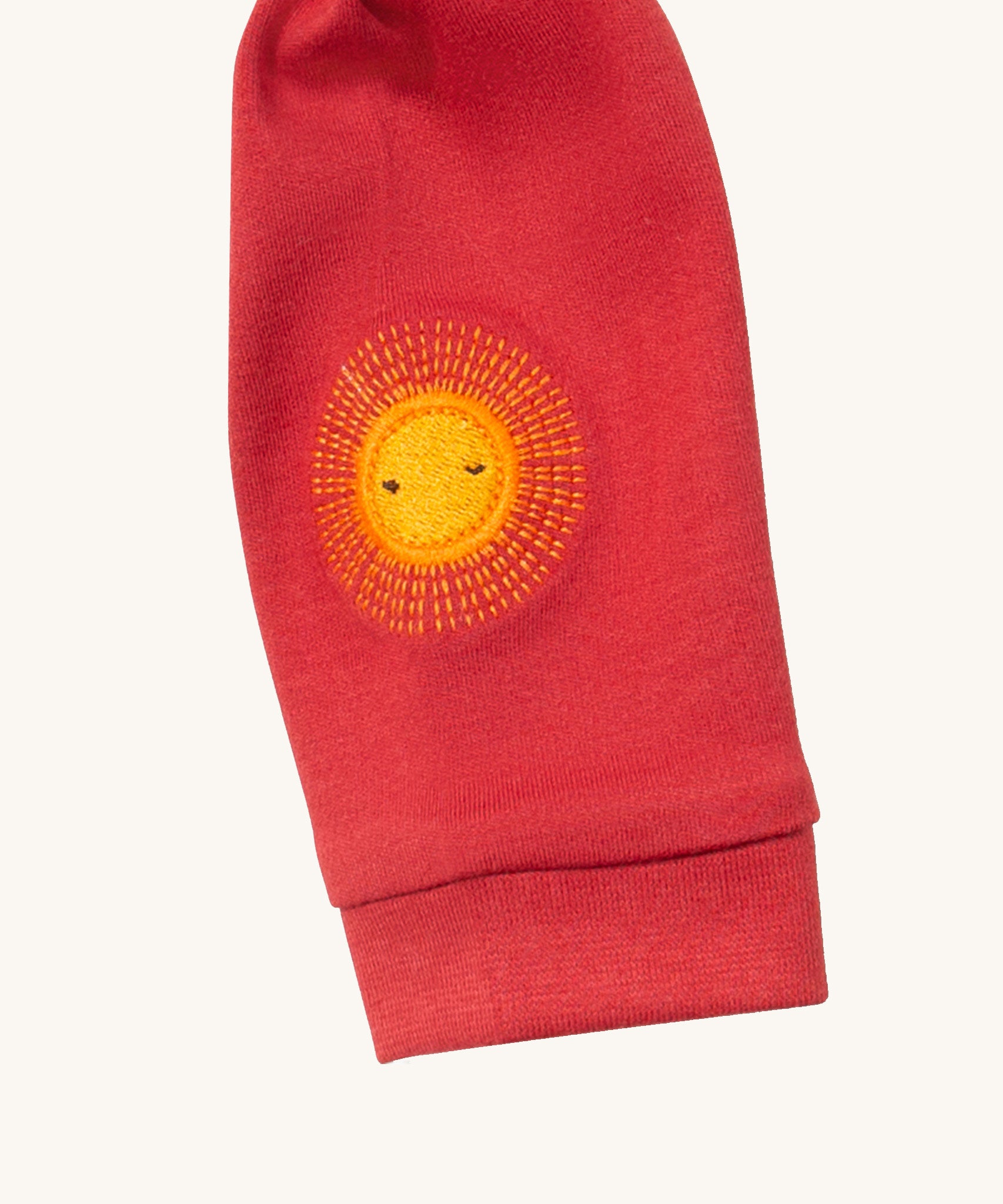 A close up of the Little Green Radicals duckling applique long sleeve top available at Babipur showing the sun embroidery detail on red organic cotton fabric.
