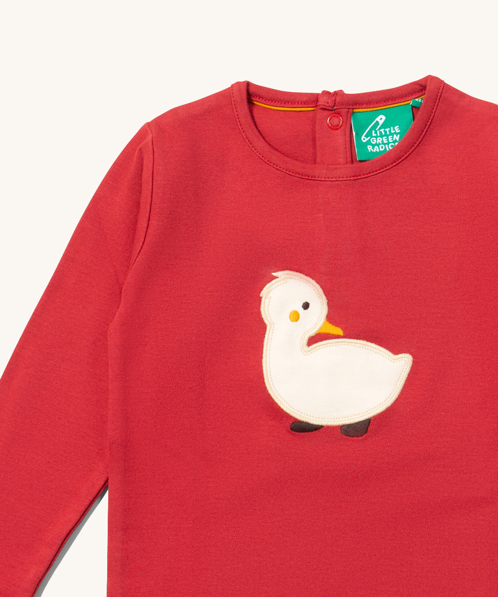 A close up of the Little Green Radicals duckling applique long sleeve top available at Babipur showing white duckling applique detail on  red organic cotton fabric.