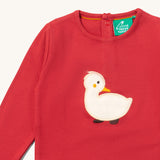 A close up of the Little Green Radicals duckling applique long sleeve top available at Babipur showing white duckling applique detail on  red organic cotton fabric.