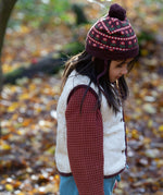Child wearing an organic knit chocolate brown hat with a red floral pattern, brown pom pom and chin straps, by Little Green Radicals, available now at Babipur.