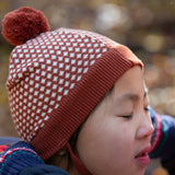 Close up of child wearing an organic cotton knit pom pom hat with ginger and cream diamon pattern, by Little Green Radicals, available to buy from Babipur. 