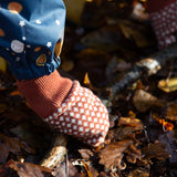 Close up of a child's hand wearing a knitted orange and cream mitten from the Little Green Radicals Autumn Winter 2025 range - made from GOTS organic and Fairtrade certified cotton, available now at Babipur.

