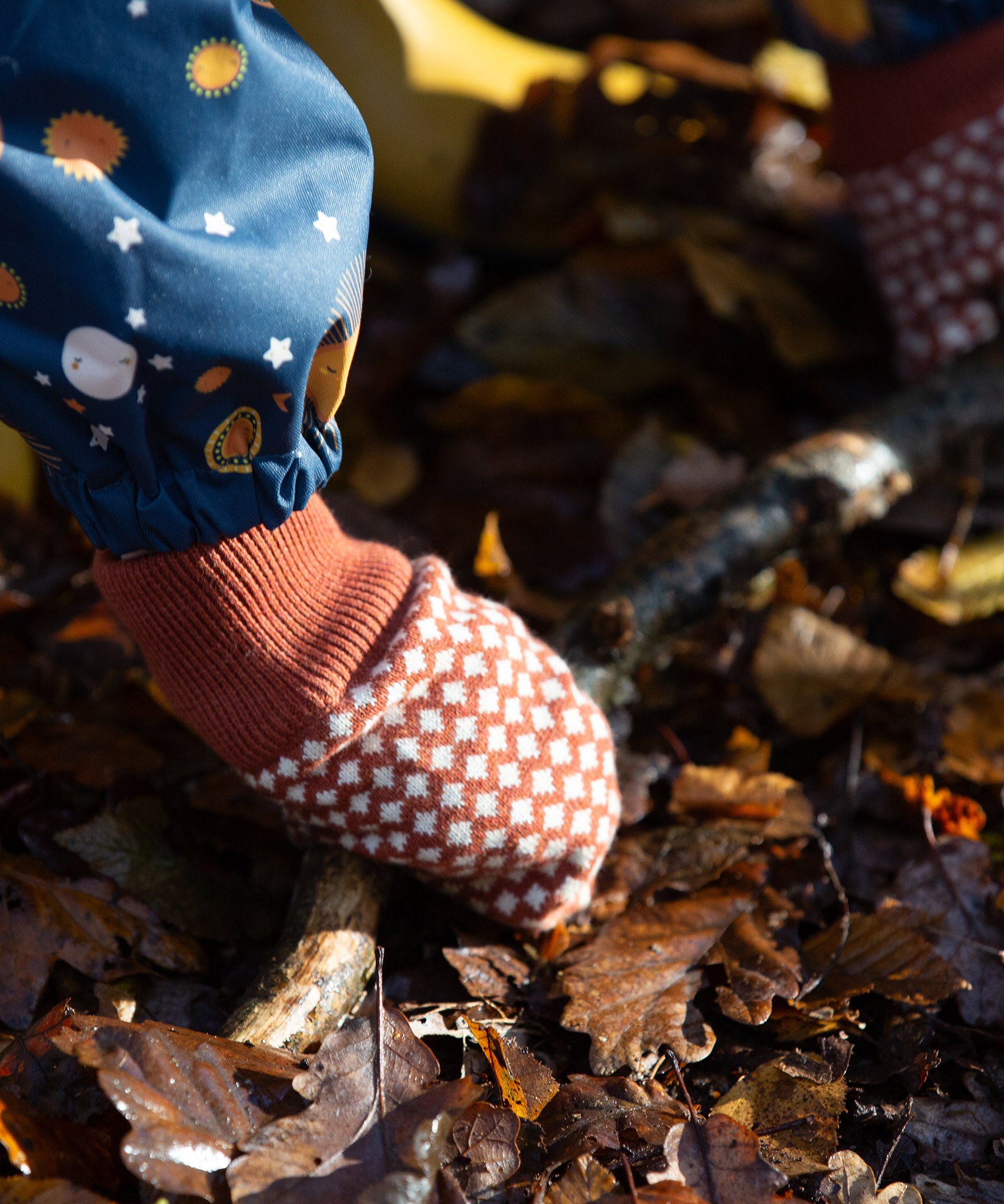 Close up of a child's hand wearing a knitted orange and cream mitten from the Little Green Radicals Autumn Winter 2025 range - made from GOTS organic and Fairtrade certified cotton, available now at Babipur.

