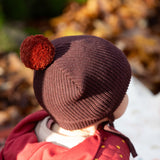 Back of baby's head wearing a Little Green Radicals knitted chocolate brown hat with a deep crimson pom pom, made from soft Fairtrade and GOTS certified organic cotton - available now at Babipur.