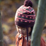 Close up of baby wearing a cosy chocolate brown knit hat with a floral pattern, brown pom pom and chin straps, made from Fairtrade GOTS organic cotton by Little Green Radicals, shop now at Babipur.