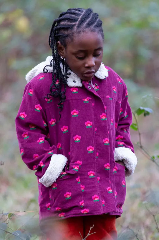 Little Green Radicals organic sherpa toasty hooded coat in plum with pink flower design worn by girl in a forest.