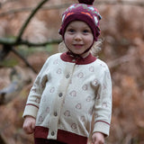 Little Green Radicals Fairtrade Organic Cotton Knitted Cardigan in Cream with Snow Penguins design and crimson cuffs, worn by child in the forest.