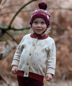 Little Green Radicals Fairtrade Organic Cotton Knitted Cardigan in Cream with Snow Penguins design and crimson cuffs, worn by child in the forest.