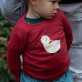 A toddler wearing the red Little Green Radicals duckling applique long sleeve top available at Babipur. 
