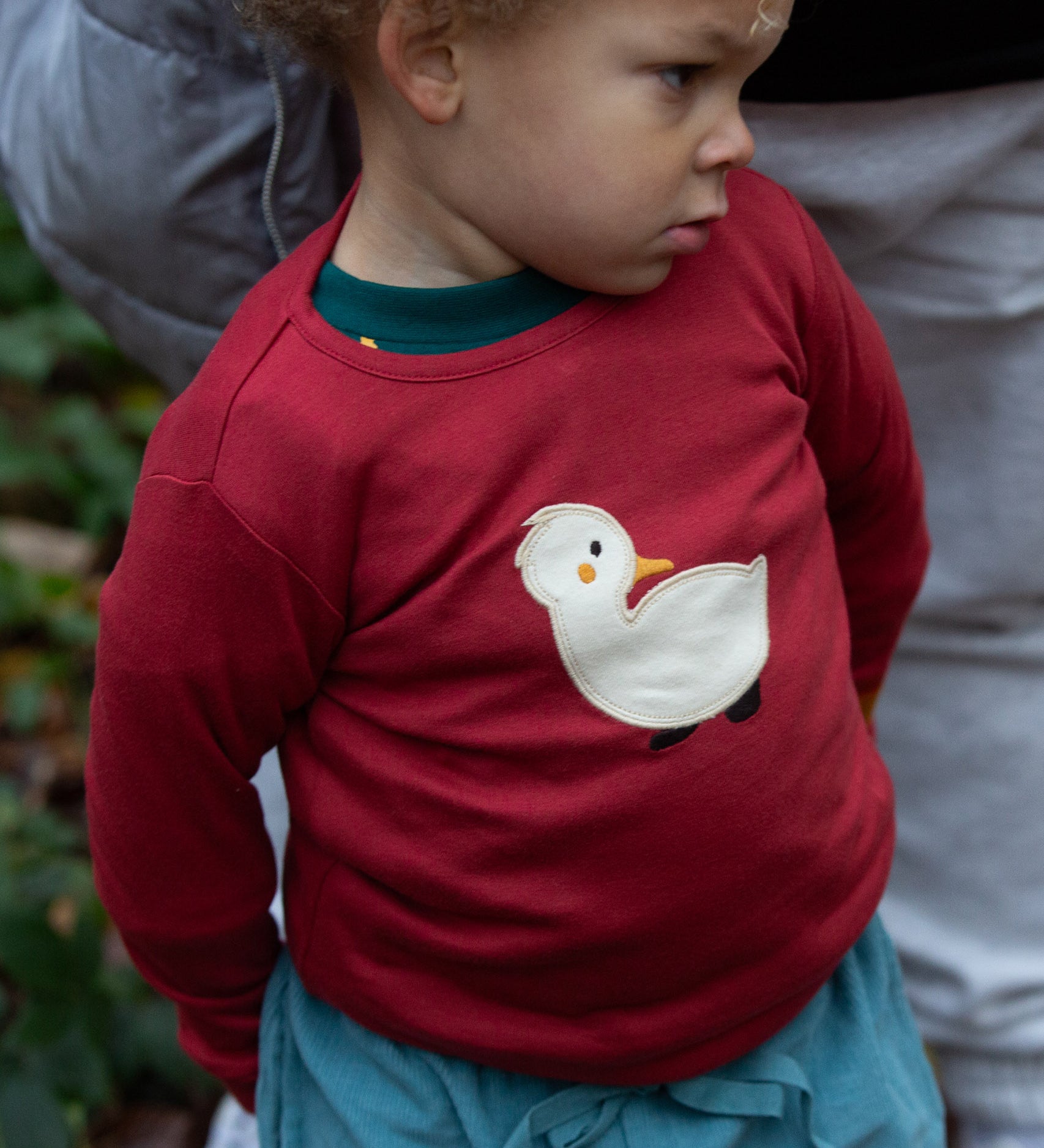 A toddler wearing the red Little Green Radicals duckling applique long sleeve top available at Babipur. 