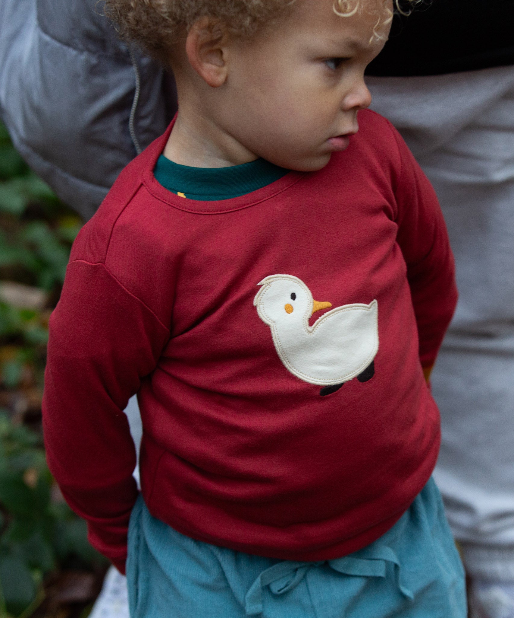 A toddler wearing the red Little Green Radicals duckling applique long sleeve top available at Babipur. 