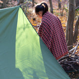 In a woodland setting, a child is snuggled in a knitted baby blanket featuring a brown and retro red floral design by Little Green Radicals — crafted from Fairtrade and GOTS-certified organic cotton, for sale at Babipur.