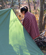 In a woodland setting, a child is snuggled in a knitted baby blanket featuring a brown and retro red floral design by Little Green Radicals — crafted from Fairtrade and GOTS-certified organic cotton, for sale at Babipur.