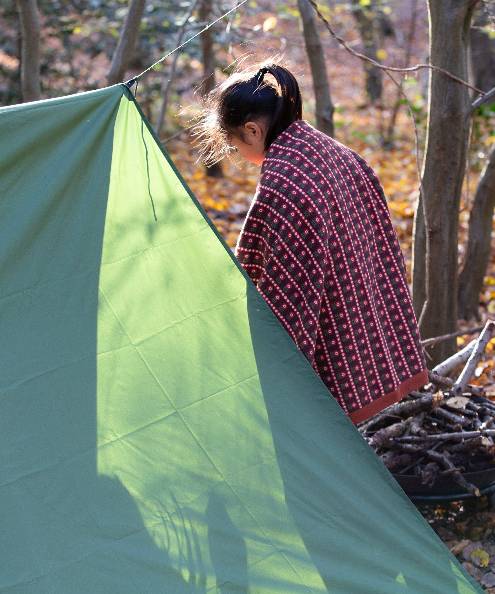 In a woodland setting, a child is snuggled in a knitted baby blanket featuring a brown and retro red floral design by Little Green Radicals — crafted from Fairtrade and GOTS-certified organic cotton, for sale at Babipur.