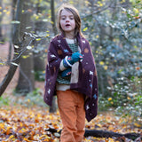 In the woods, a child is wrapped in a cosy brown baby blanket decorated with flying birds, designed by Little Green Radicals and made from Fairtrade and GOTS-certified organic cotton, for sale at Babipur.