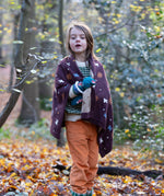 In the woods, a child is wrapped in a cosy brown baby blanket decorated with flying birds, designed by Little Green Radicals and made from Fairtrade and GOTS-certified organic cotton, for sale at Babipur.