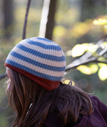 Side of child's head wearing a blue and cream striped knitted beanie with a red trim by Little Green Radicals - made with Fairtrade certified and GOTS organic cotton - available now at Babipur.
