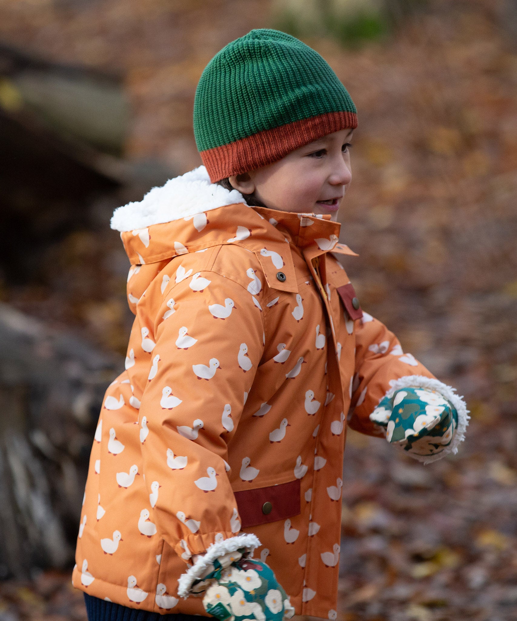 Child running through a forest wearing a chive green with a crimson trim Knit Beanie by Little Green Radicals with a red trim and matching scarf - made from soft GOTS organic and Fairtrade certified cotton - for sale at Babipur.