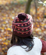 Back of child wearing an organic and Fairtrade knitted chocolate brown hat with a red floral pattern, brown pom pom, by Little Green Radicals, for sale at Babipur.