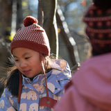 Close up of child wearing a Fairtrade orange and cream diamond patterned organic cotton knit pom pom hat, by Little Green Radicals, for sale at Babipur.