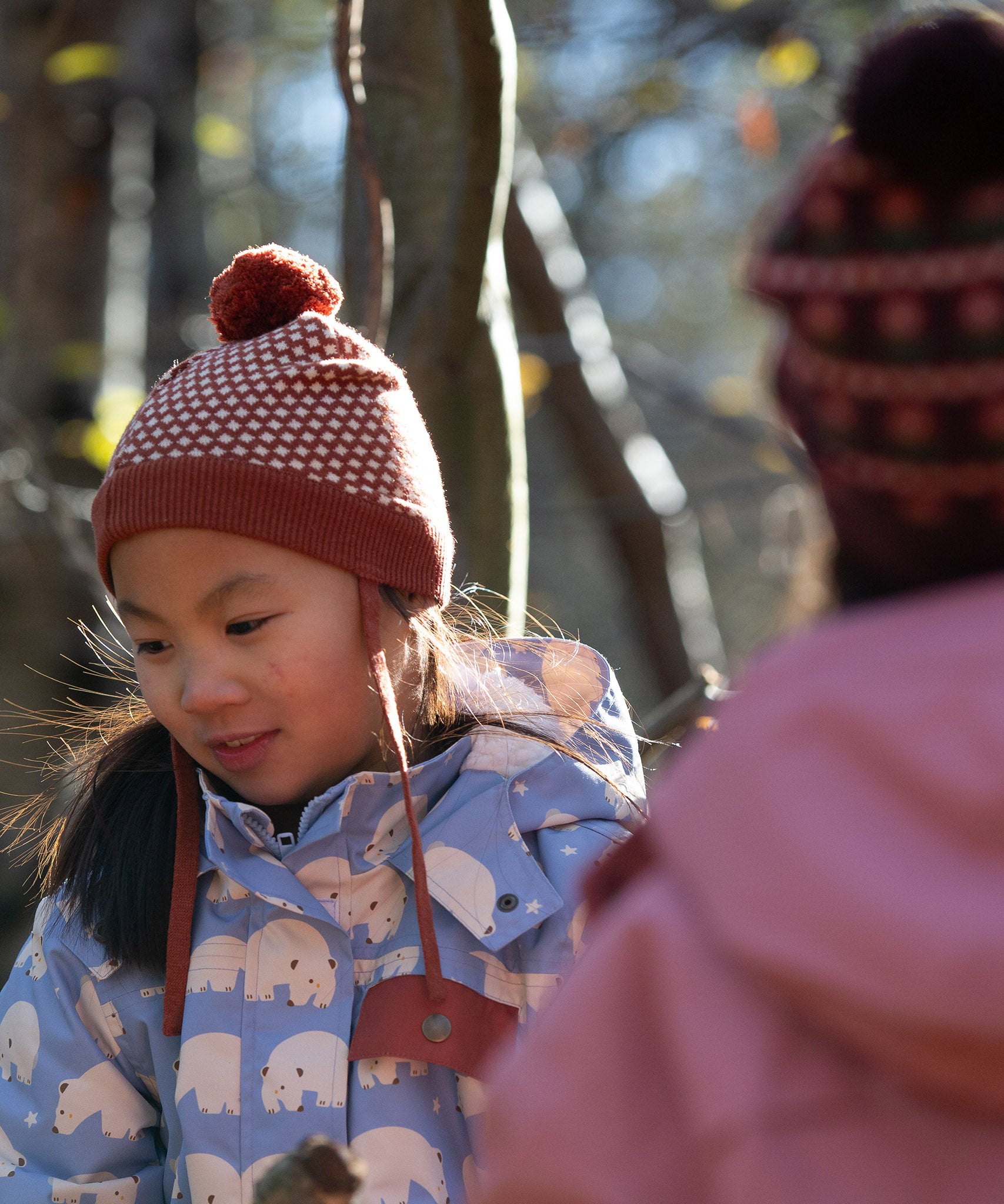 Close up of child wearing a Fairtrade orange and cream diamond patterned organic cotton knit pom pom hat, by Little Green Radicals, for sale at Babipur.