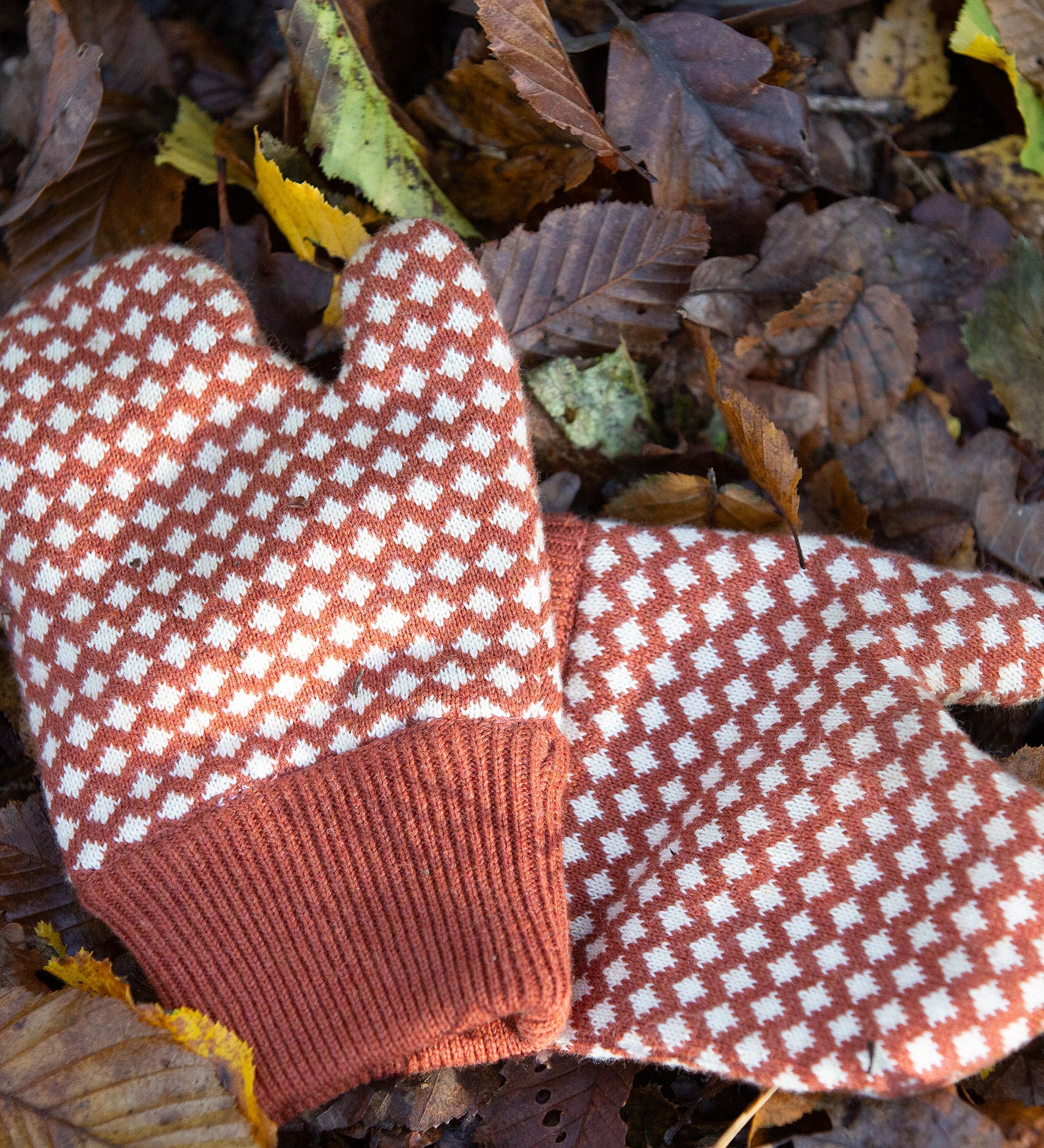 Close up of a pair of Little Green Radicals Knitted Mittens with a Ginger Orange and Cream Diamond Pattern - made from soft Fairtrade certified and GOTS organic cotton - with thick orange cuffs - available to buy at Babipur.