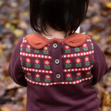 A close up of a child wearing the dark maroon Little Green Radicals collecting flowers knitted collar dress showing the button fastener detail on the back of the dress