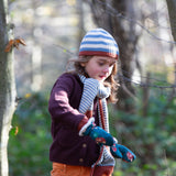Child running through a forest wearing a striped blue and cream Knit Beanie by Little Green Radicals with a red trim and matching scarf - made from soft GOTS organic and Fairtrade certified cotton - available to buy at Babipur.
