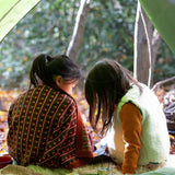 A child in the forest is wrapped in a brown and retro red floral patterned knitted baby blanket by Little Green Radicals, made from Fairtrade and GOTS-certified organic cotton, available at Babipur.