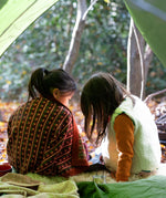 A child in the forest is wrapped in a brown and retro red floral patterned knitted baby blanket by Little Green Radicals, made from Fairtrade and GOTS-certified organic cotton, available at Babipur.
