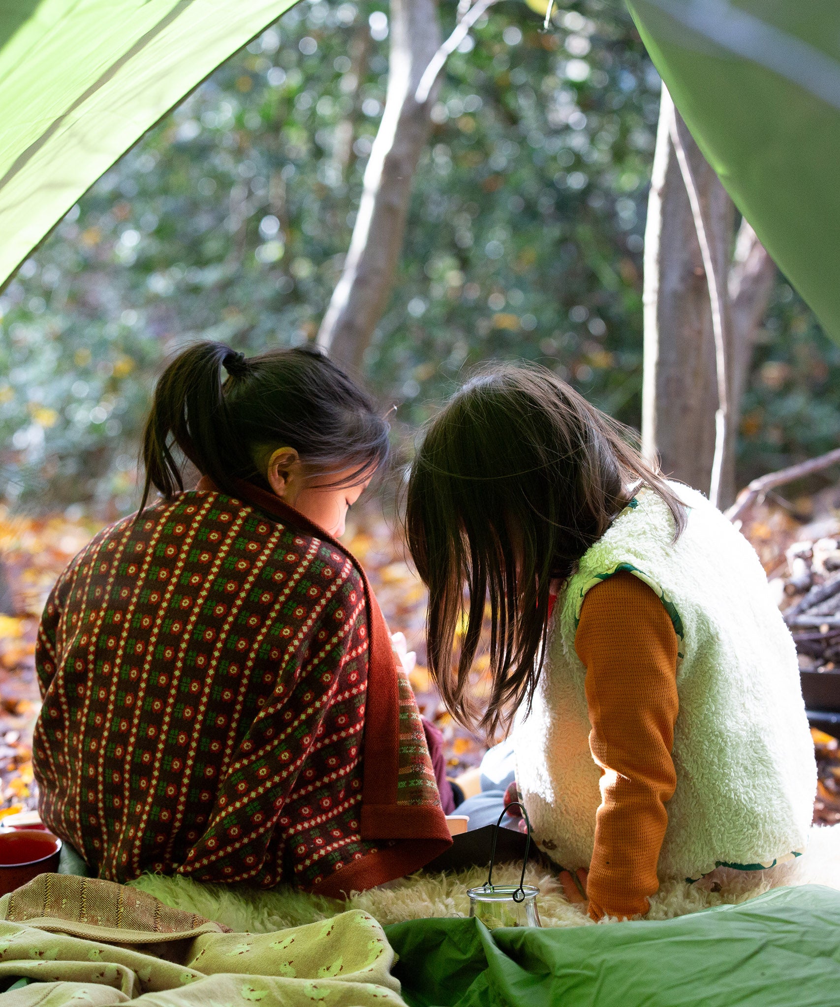 A child in the forest is wrapped in a brown and retro red floral patterned knitted baby blanket by Little Green Radicals, made from Fairtrade and GOTS-certified organic cotton, available at Babipur.
