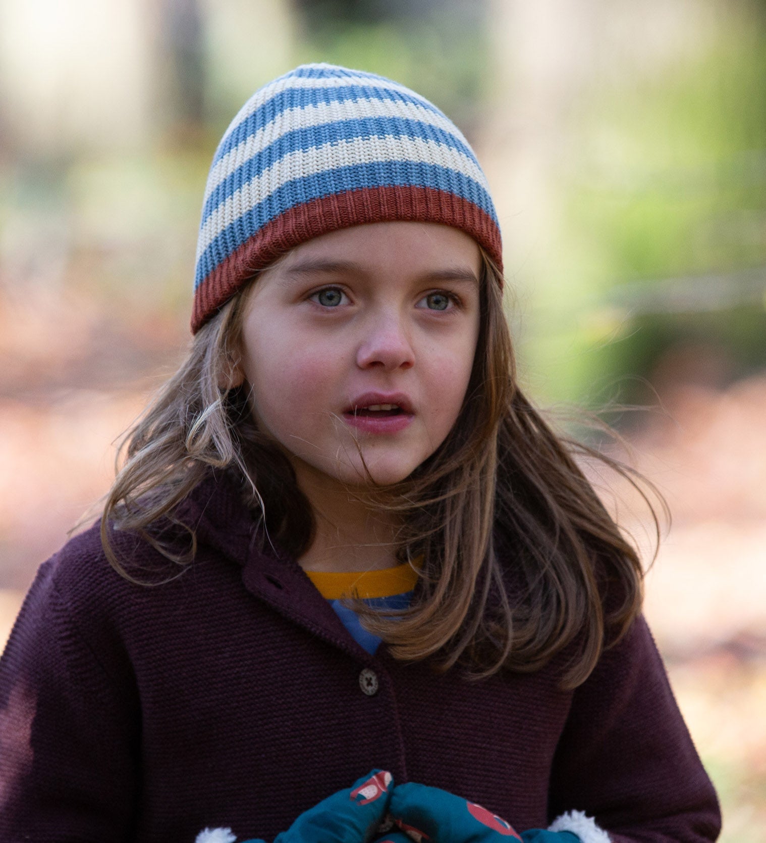 Close up of a child wearing a knitted beanie hat in cream and blue stripes made from soft Fairtrade and GOTS certified organic cotton by Little Green Radicals - for sale at Babipur.