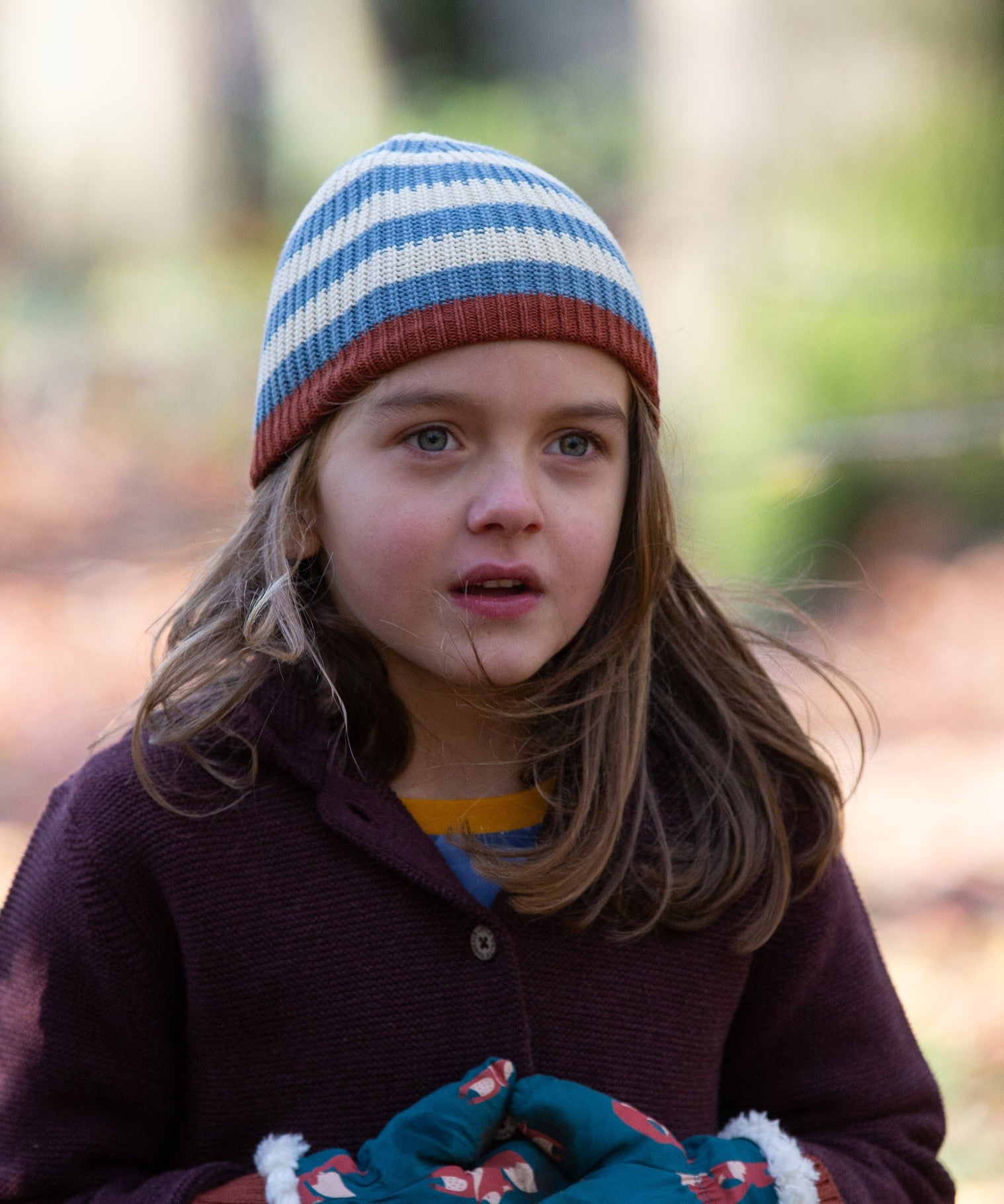 Close up of a child wearing a knitted beanie hat in cream and blue stripes made from soft Fairtrade and GOTS certified organic cotton by Little Green Radicals - for sale at Babipur.