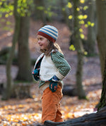 Child stood in a forest wearing a blue and cream striped Knitted Beanie by Little Green Radicals with a red trim - made from soft GOTS organic and Fairtrade certified cotton - for sale at Babipur.