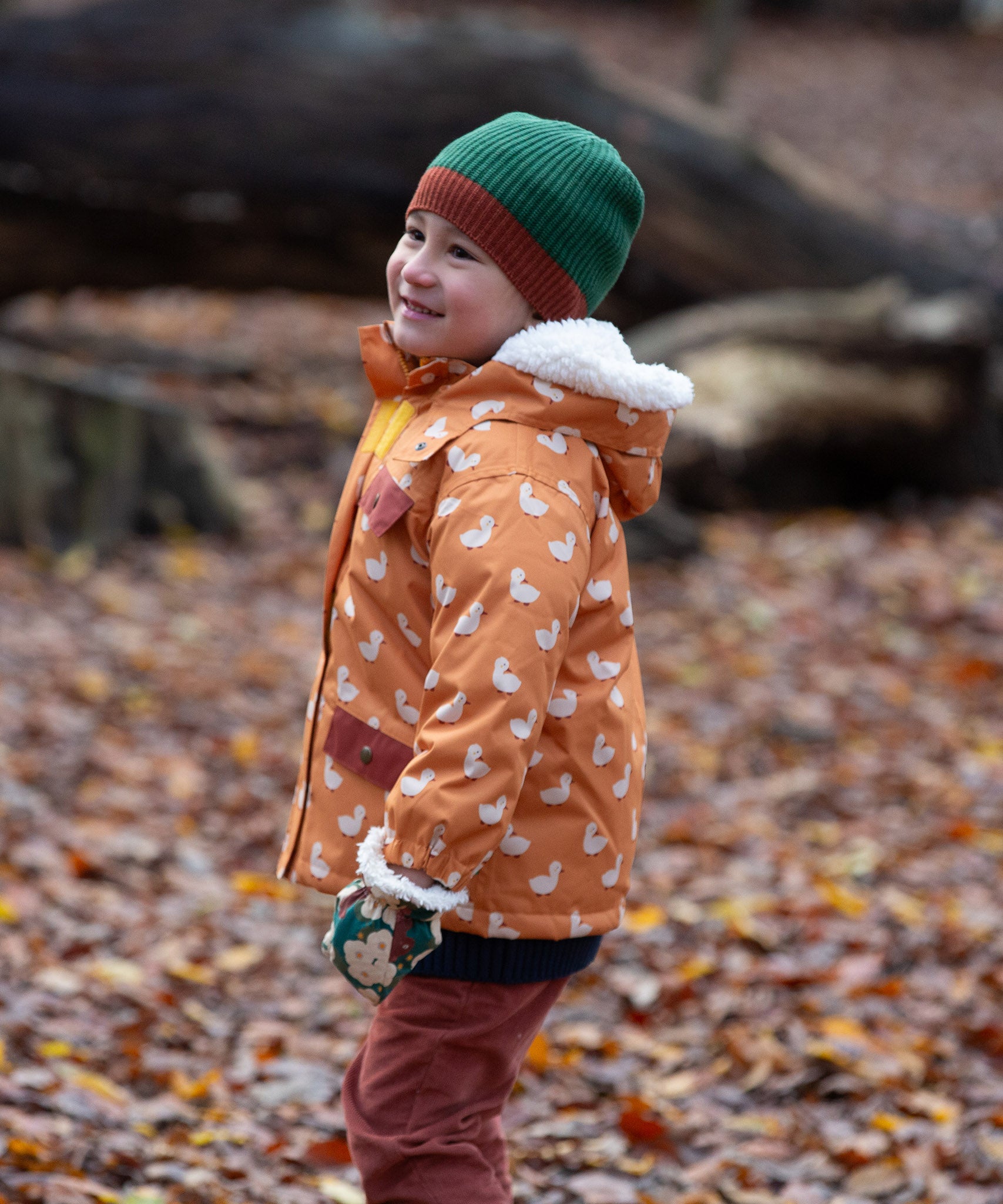 Child in a forest wearing Knit Beanie in chive green with a crimson trim by Little Green Radicals - made from soft GOTS organic and Fairtrade certified cotton - shop now at Babipur. 