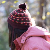 Side of child wearing a knitted brown hat with a red floral pattern and a brown pom pom, by Little Green Radicals, made from soft Fairtrade and GOTS certified organic cotton - shop now at Babipur.