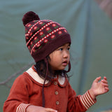 Close up of baby wearing a Little Green Radicals cosy chocolate brown knit hat with a floral pattern, brown pom pom and chin straps, made from Fairtrade GOTS organic cotton, available now at Babipur.