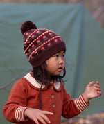 Close up of baby wearing a Little Green Radicals cosy chocolate brown knit hat with a floral pattern, brown pom pom and chin straps, made from Fairtrade GOTS organic cotton, available now at Babipur.