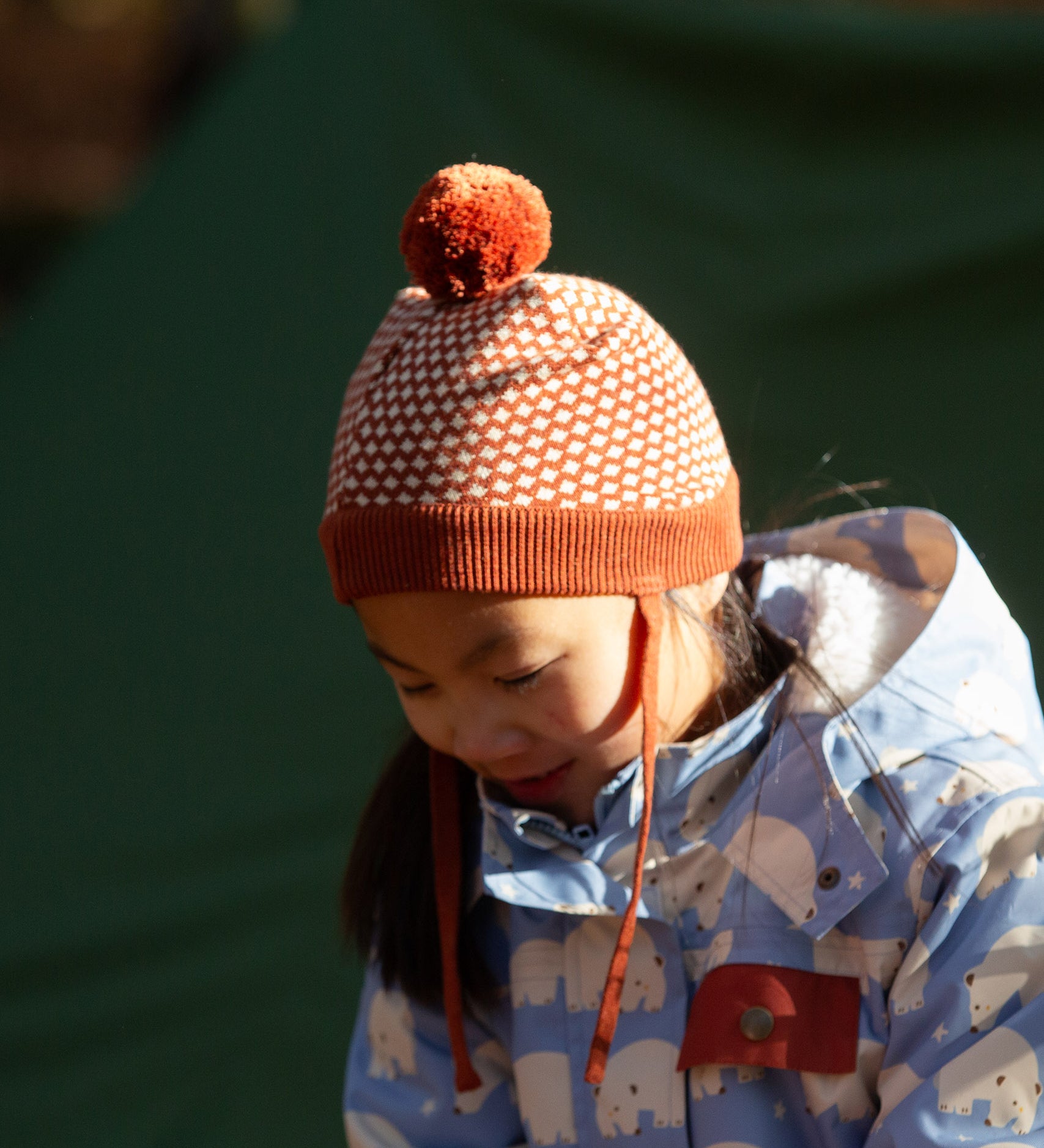 Child wearing an organic and Fairtrade Little Green Radicals knitted pom pom hat with an orange and cream pattern, for sale at Babipur.