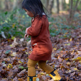 Child playing in a forest wearing a Long Sleeve Orange Ginger Knitte Dress by Little Green Radicals - made from soft GOTS organic and Fairtrade certified cotton - with striped cream and orange cuffs.
