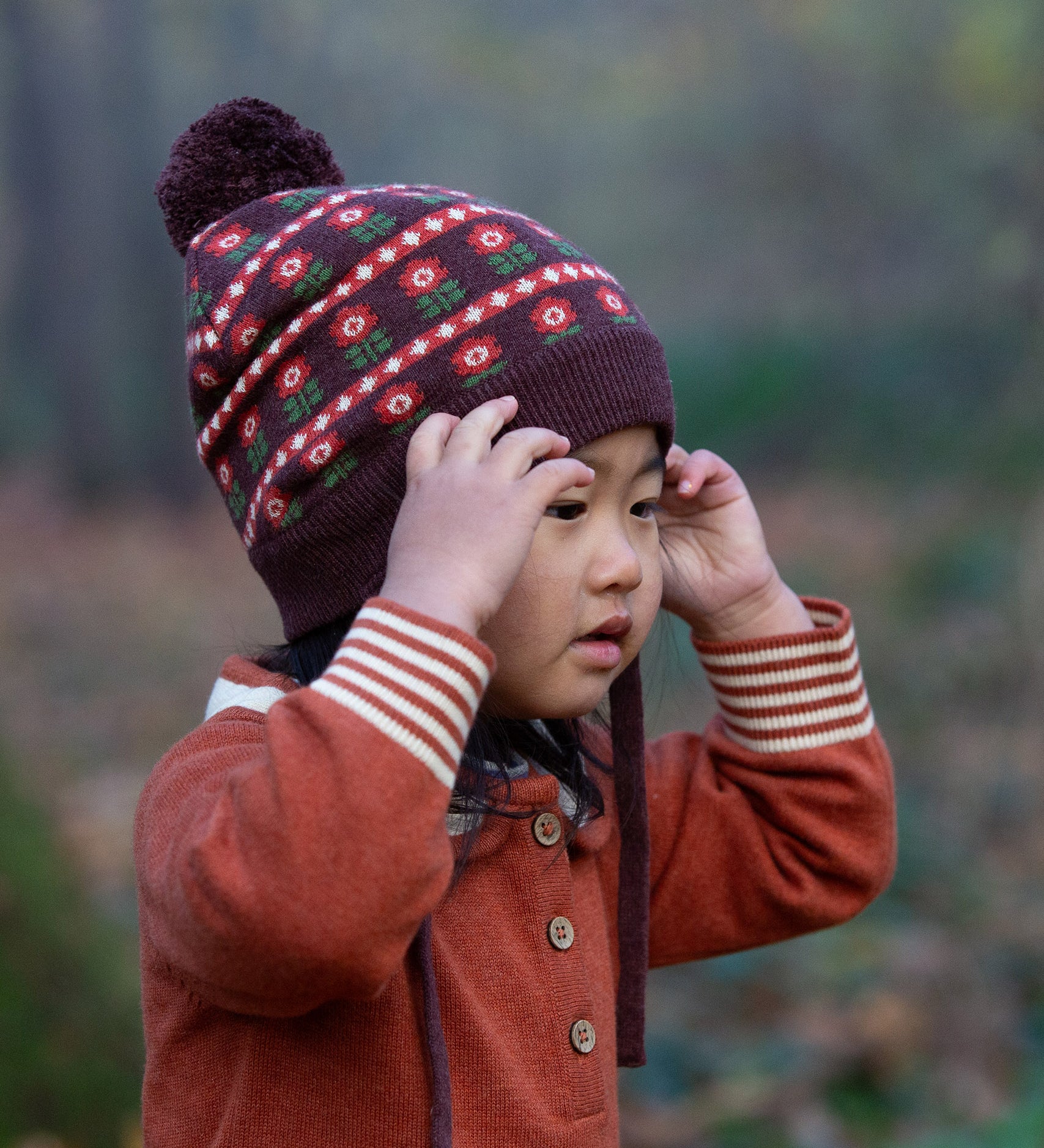 Close up of child in a forest wearing Little Green Radicals Long-Sleeve Knitted Collar Dress in Ginger Orange - made from soft Fairtrade certified and GOTS organic cotton - with striped cream and orange cuffs and three wooden buttons - available to buy at Babipur.