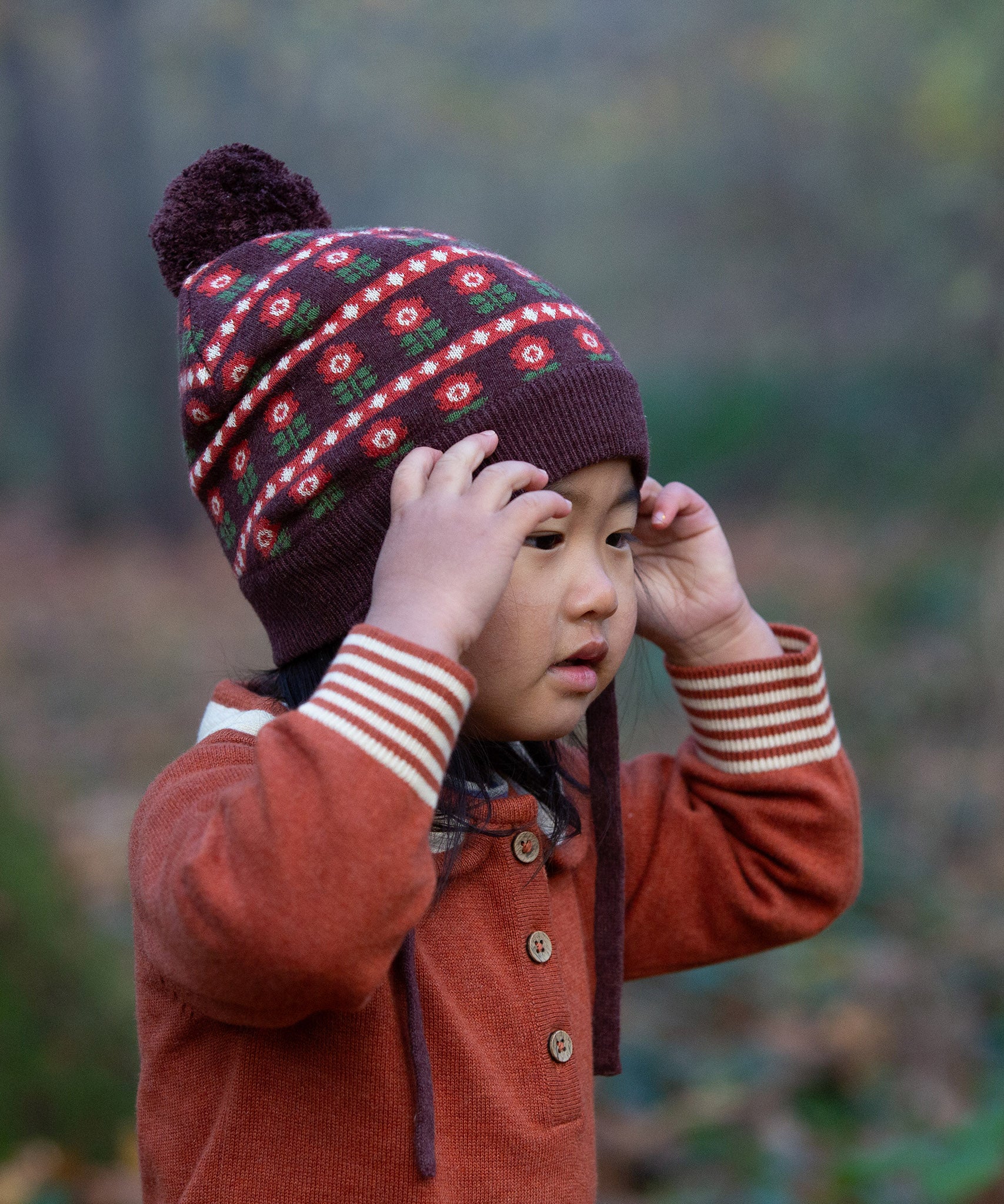 Close up of child in a forest wearing Little Green Radicals Long-Sleeve Knitted Collar Dress in Ginger Orange - made from soft Fairtrade certified and GOTS organic cotton - with striped cream and orange cuffs and three wooden buttons - available to buy at Babipur.