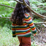 A child walking through woodland and wearing the Little Green Radicals rainbow waffle snuggly knitted jumper