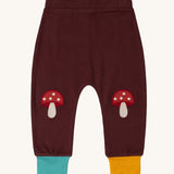 Little Green Radicals knee patch joggers in toadstool design available at Babipur. A GOTS organic cotton jogger in dark maroon with blue and yellow leg cuffs. Features toadstool applique kneepatches 